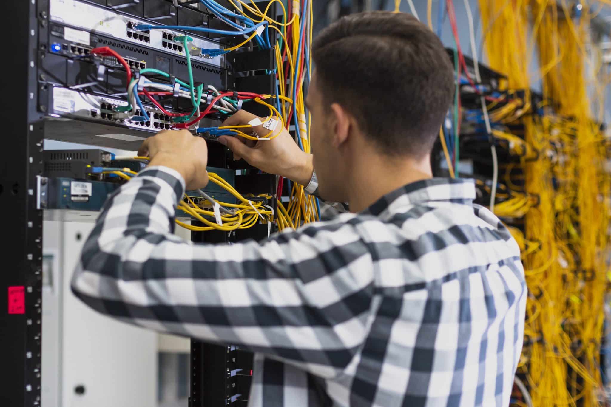 Technician connecting patch leads to Ethernet switches in a business network cabinet